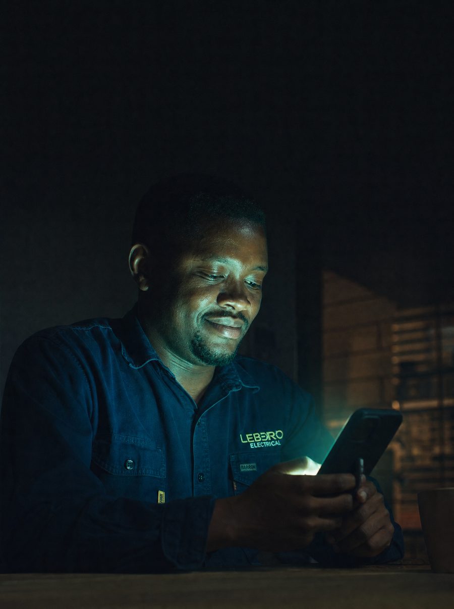 A South African electrician at home late at night, smiling at a job booked on his phone while he rested